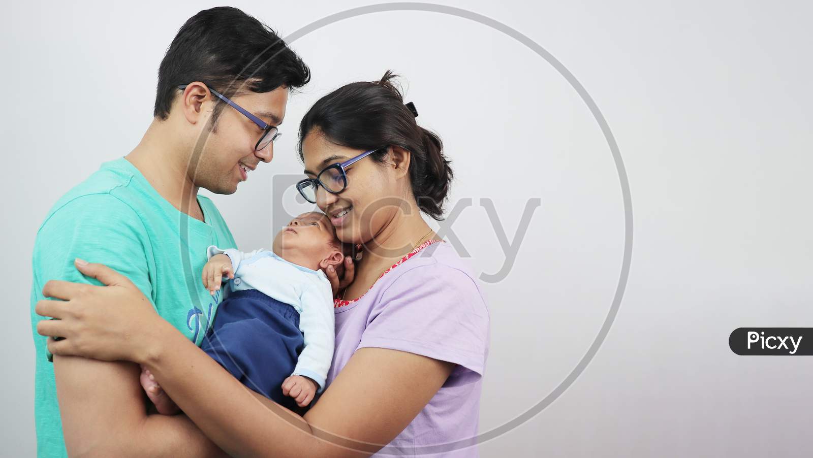 A Young Man With His Wife And Newborn Kid Looking At The Baby Isolated In White Background.