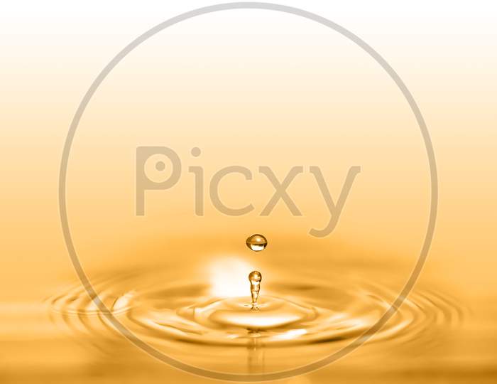 Closeup On Drop Of Cosmetic Golden Oil Liquid Creating A Circular Wave.