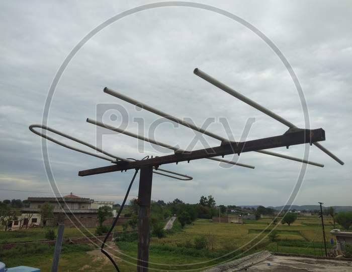 A TV antenna with cloudy sky and village background