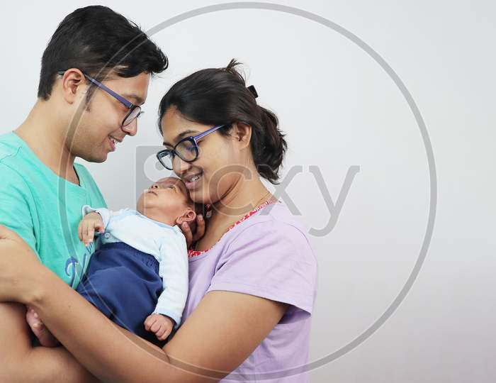 A Young Man With His Wife And Newborn Kid Looking At The Baby Isolated In White Background.