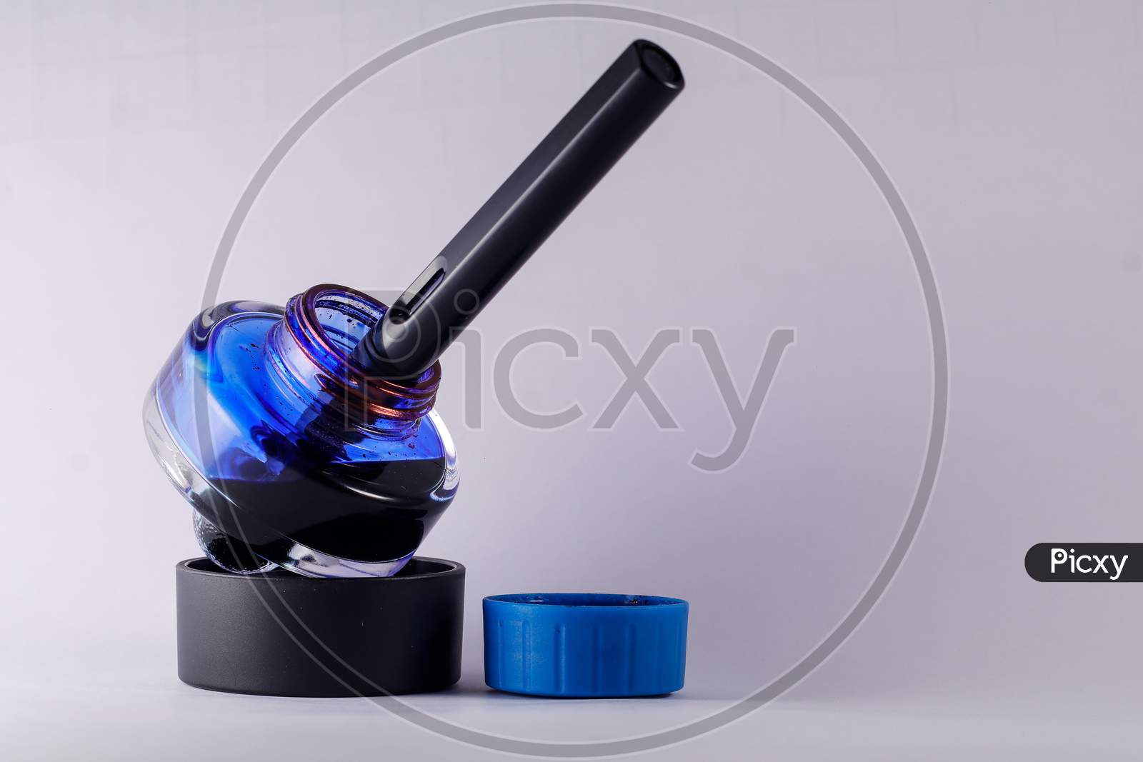 A View Of Open Blue Ink Bottle With A Fountain Pen Dip Inside Against White Background