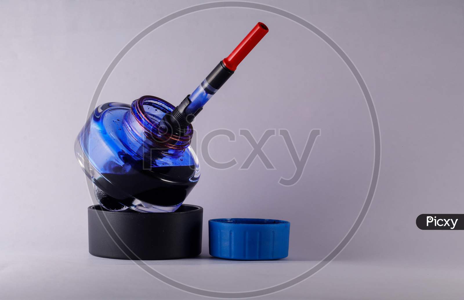A View Of Open Blue Ink Bottle With A Refilling Fountain Pen Dip Inside Against White Background