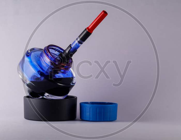 A View Of Open Blue Ink Bottle With A Refilling Fountain Pen Dip Inside Against White Background