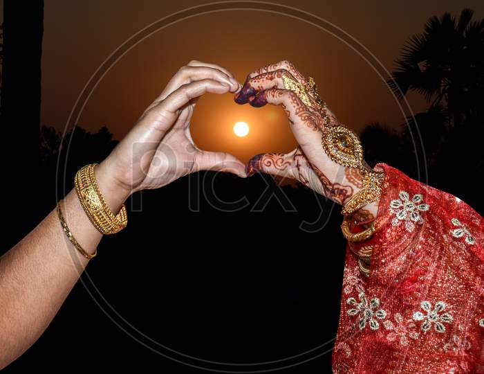 Two women’s Hands forming a heart shape with sunset silhouette