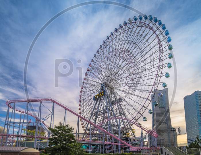 View From Kokusai Bridge Of Cosmo Clock 21 Big Wheel At Cosmo World Theme Park, Overlooking The Diving Coaster Vanish In The Minato Mirai District Of Yokohama With The Landmark Tower In The Sunset Summer Sky.