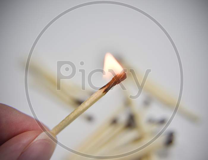 Burning Wooden Match In The Hand With Matches On The White Backgtound. Selective Focus. Chain Reaction Concept.
