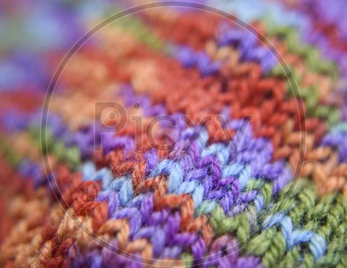 Selective Focus At The Bright Colorful Knitted Pattern Close-Up Look. Natural Wool Of Red, Orange, Green, Blue, Purple Colors.
