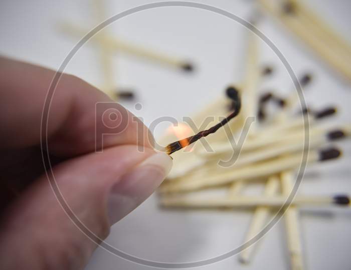 Burning Wooden Match In The Hand With Matches On The White Backgtound. Selective Focus. Chain Reaction Concept.
