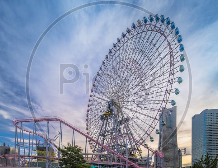 View From Kokusai Bridge Of Cosmo Clock 21 Big Wheel At Cosmo World Theme Park, Overlooking The Diving Coaster Vanish In The Minato Mirai District Of Yokohama With The Landmark Tower In The Sunset Summer Sky.