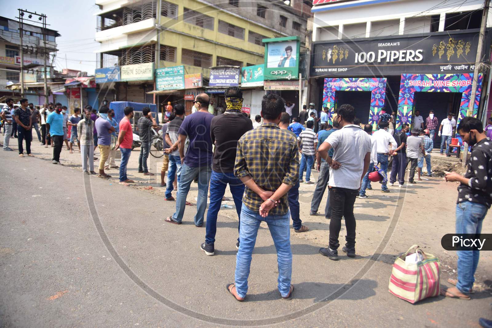 People Maintain Social Distance As They Stand In A Queue Outside A Wine Shop, During The Nationwide Lockdown To Curb The Spread Of Coronavirus or Covid-19 , In Nagaon District Of Assam Monday, April 13, 2020.