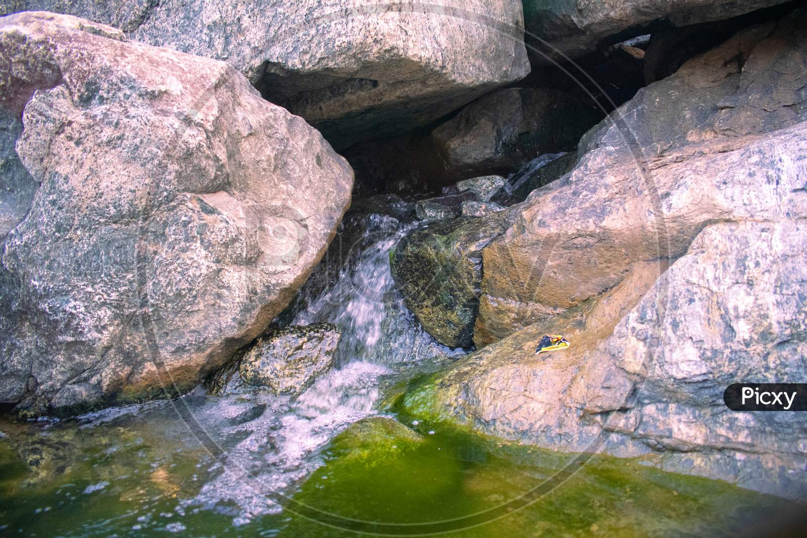 Water Flowing Out From The Rocks With Green Moss On The Sides