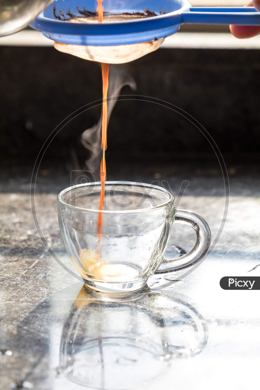 Steamy Masala Tea Being Poured Into A Transparent Glass Cup