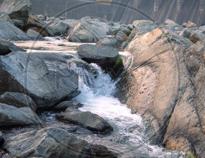 Water Flowing Between The Big Rocks Forming A Small Waterfall