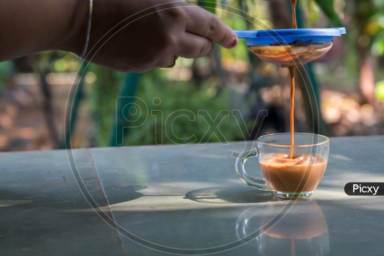 A Hand Pouring Steamy Masala Tea Through Plastic Strainer Into A Glass Cup