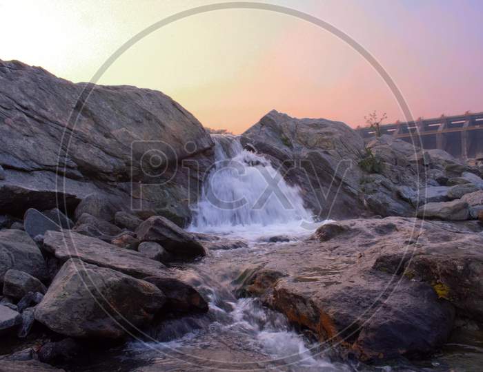 A Small Waterfall Flowing Between The Rocks During Sunset