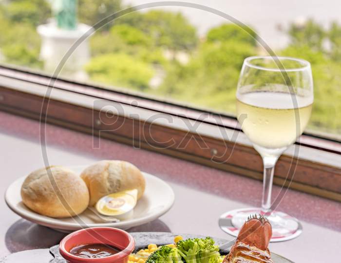 Minced Beef And Seafood Lobster Tail With Cheese, Corn,Broccoli,Bread On Plate And White Wine With The Replica Of The Statue Of Liberty In Odaiba In Background.