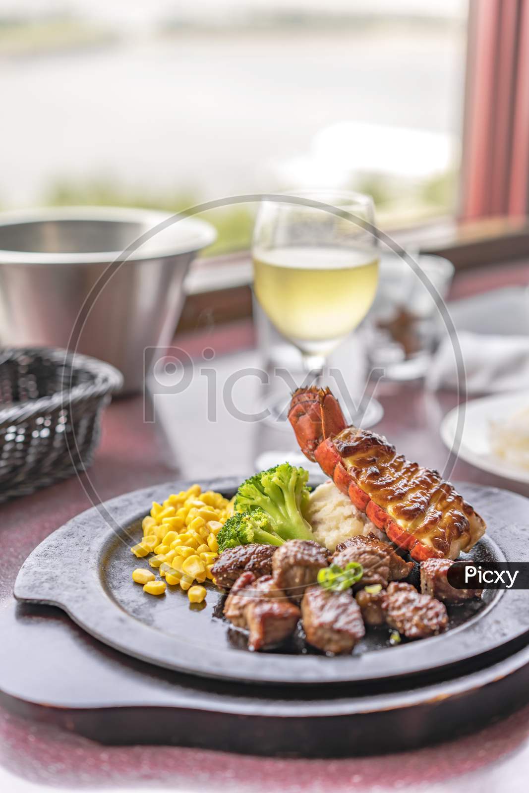 Beef Steack And Seafood Lobster Tail With Cheese, Corn And Broccoli On Plate With White Wine In Glass.