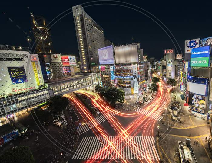 Aerial View Of The Shibuya Crossing Intersection In Front Of Shibuya Station On A Summer Night With The Speed Lights Flow Of Cars.