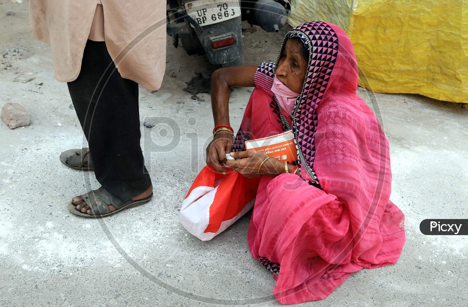 An Old Woman Sitting  In A Queue Line To Withdraw Money  Outside Of A Bank During A Nationwide Lockdown To Slow The Spreading Of The Coronavirus Disease (Covid-19), In Prayagraj, April, 16, 2020.