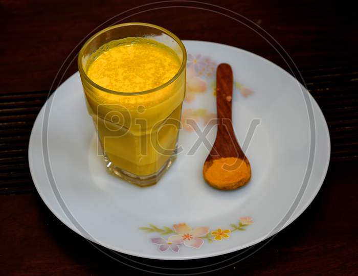 Turmeric Milk in a Glass With a Spoon of Turmeric Powder