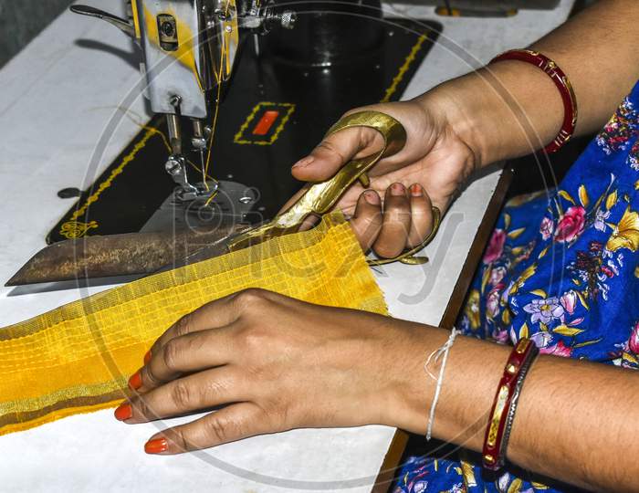 Ladies tailor of India cutting clothes with scissors and making dress by sewing machine