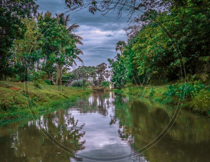 water canal passing through a forest and cloudy sky