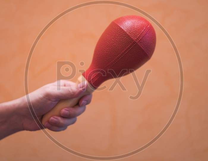 Close-Up Of A Man'S Hand Holding A Red Maraca On An Orange Background.