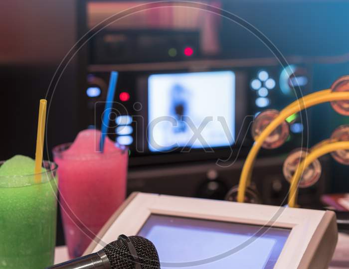 Black Microphone In Karaoke Club, With Remote Controller, Melon And Strawberry Soda Drinks, Yellow Tambourine And Screen For Singing Music On Stage Party.