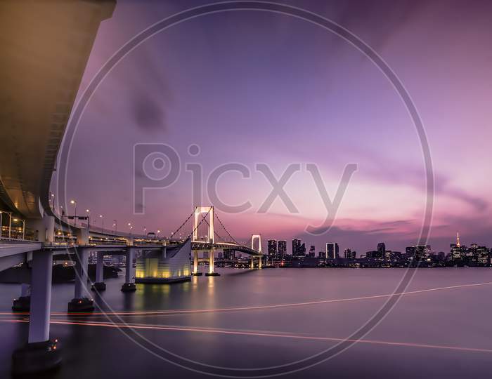 Long Exposure Photography Of Sunset On Rainbow Bridge And Tokyo Bay In Background.