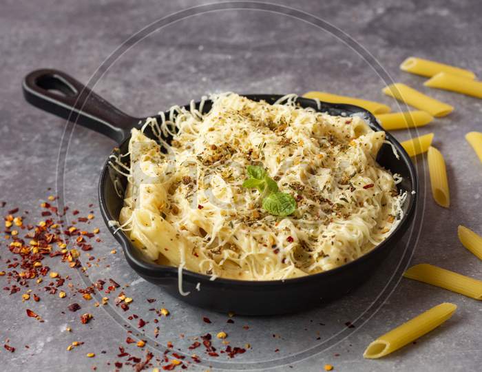 Cheese white sauce penne pasta served in pan with cheese shredded on top