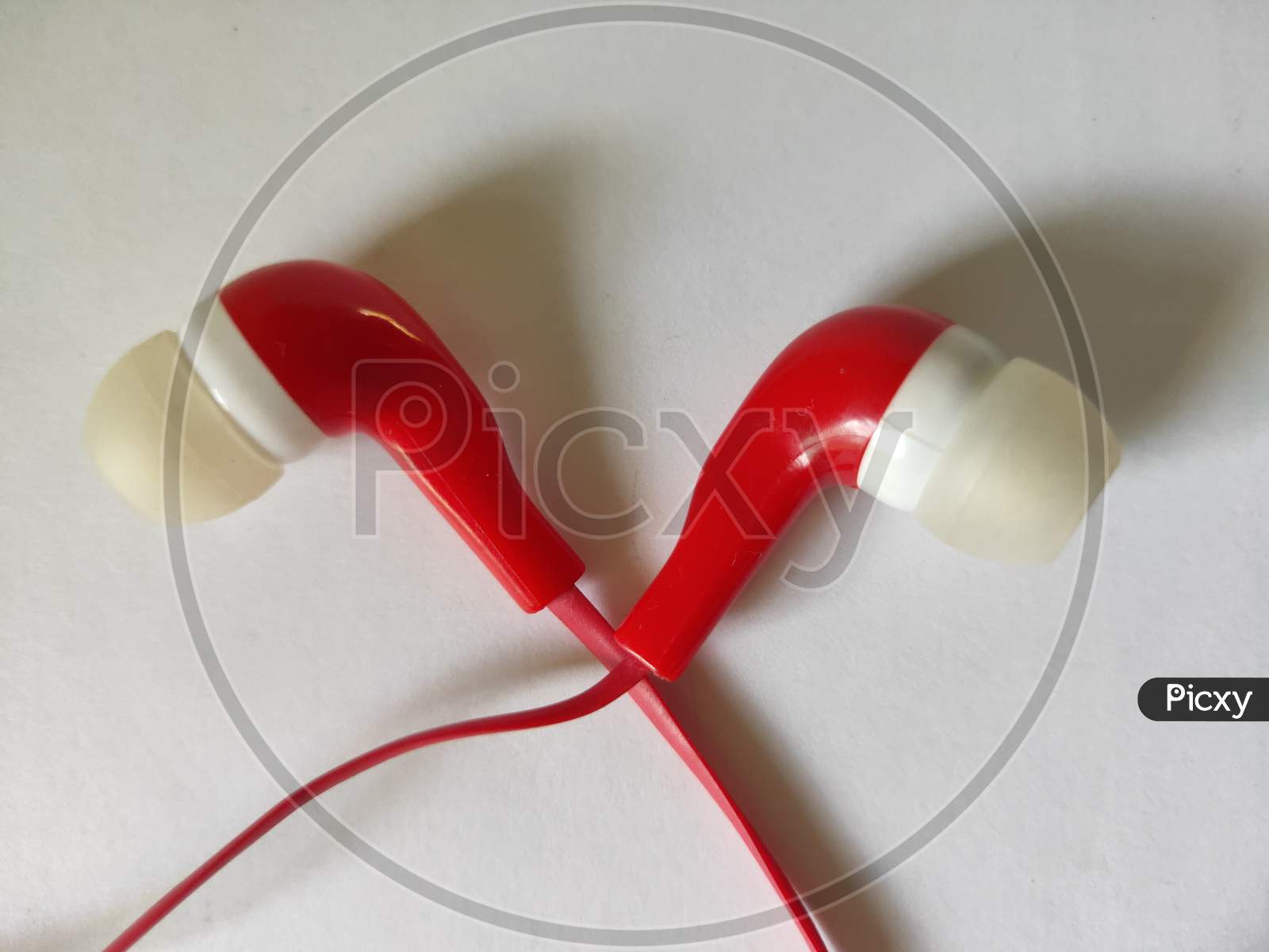 Earphones on white background. Red earphones on plain background. Headphones and heart shaped object. Listen to heart through headphones.