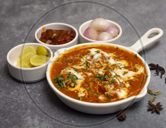 Tasty butter chicken curry dish served with lemon, onion and mango pickle - an Indian cuisine