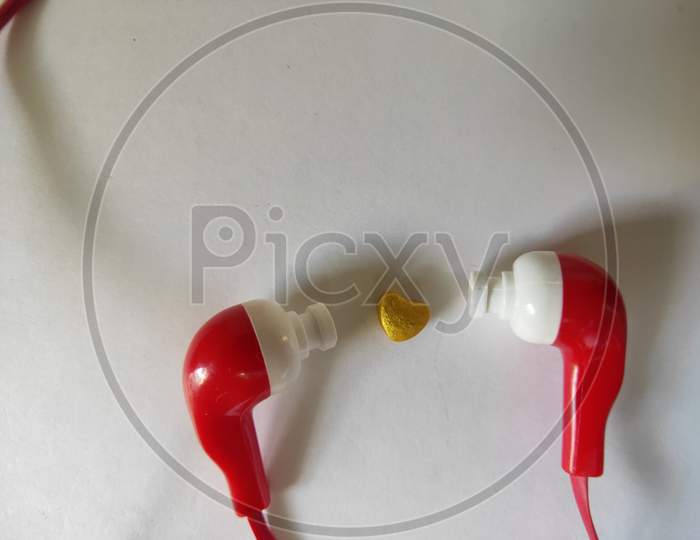 Earphones on white background. Red earphones on plain background. Headphones and heart shaped object. Listen to heart through headphones.