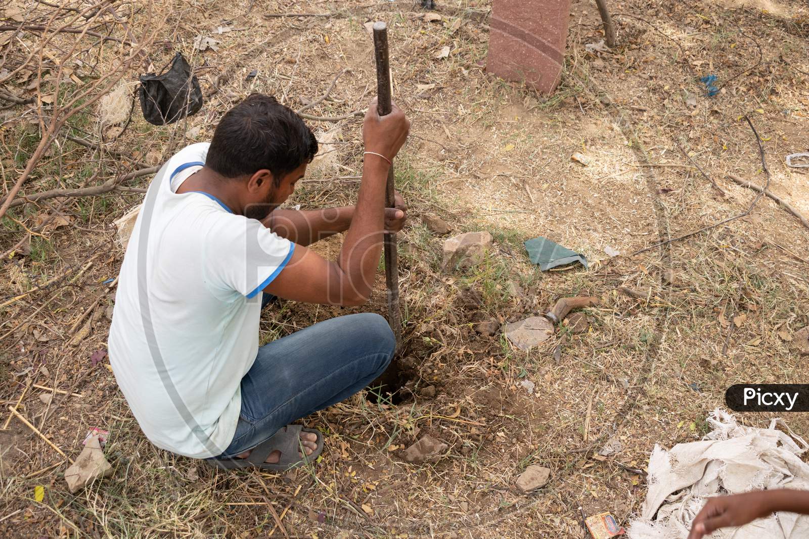 A man digging a hole using an iron crowbar