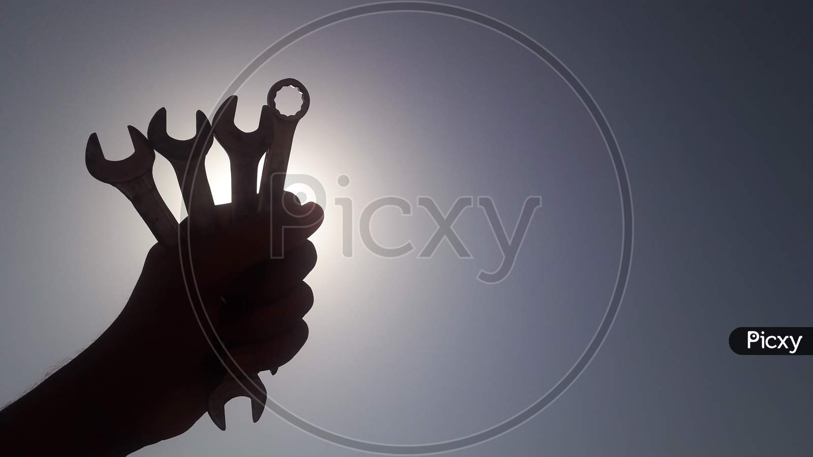 A worker is holding wrench in his hand tightly in front of the sun in blue sky, labours day or workers day