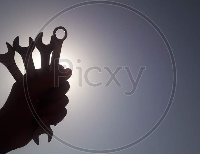 A worker is holding wrench in his hand tightly in front of the sun in blue sky, labours day or workers day