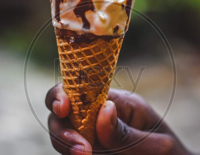 Boy Hand Holding A Butterscotch Ice Cream Cone With Cashew Nuts Ice Cream On A Nature Background.