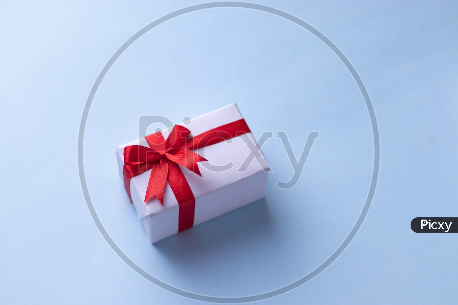 White gift box with red ribbon, blue background flat lay for stock image