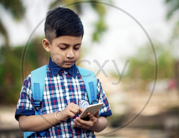 Smiling young male kid using digital smartphone watching online e-learning video to studying in classroom , Asian Indian schoolboy study with Mobile phone.