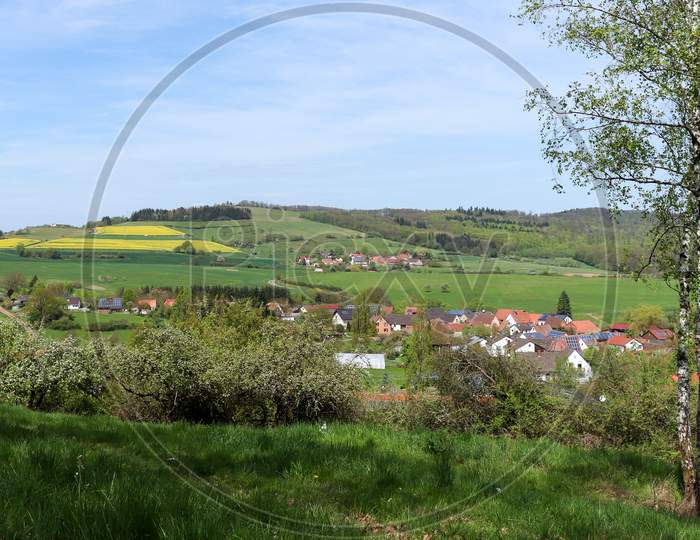 Rooftops Of The Germany Village, Potzbach. Field Of Rapeseed On The Hill In The Background On A Spring Day.