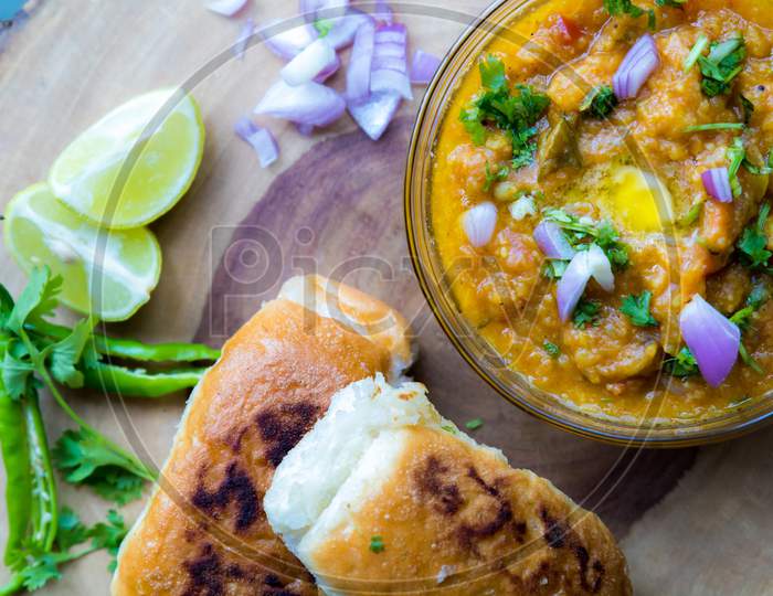 Famous Indian Street Food Pav Bhaji Decorated On A Wooden Plate On Gray Background And Garnished With Raw Onion Lemon Coriander And Green Chillies