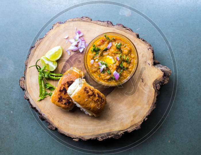 Famous Indian Street Food Pav Bhaji Decorated On A Wooden Plate On Gray Background And Garnished With Raw Onion Lemon And Green Chillies