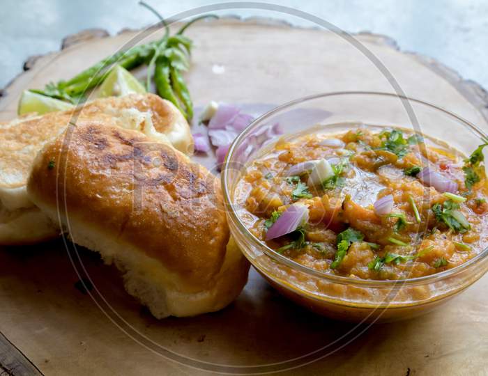 Famous Indian Street Food Pav Bhaji Decorated On A Wooden Plate On Gray Background And Garnished With Raw Onion Lemon Coriander And Green Chillies