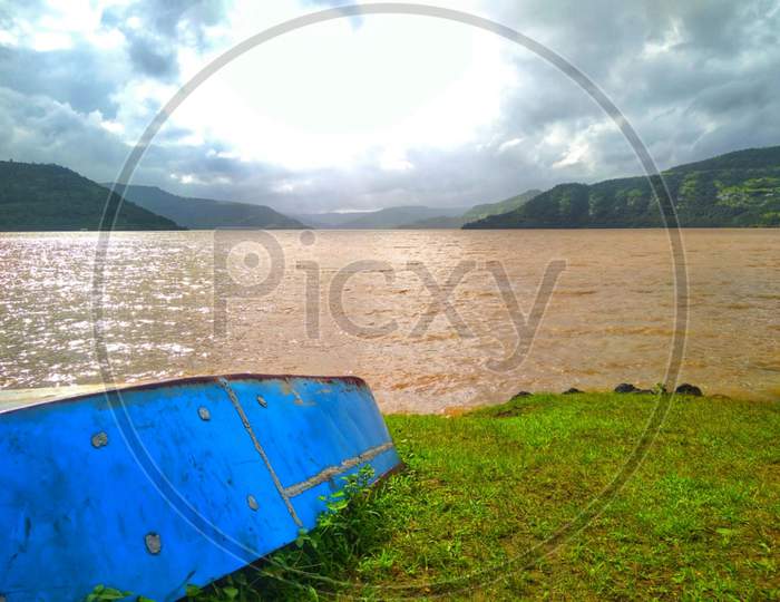 View of very beautiful backwater of dam with blue boat on shore and clouds with mountains