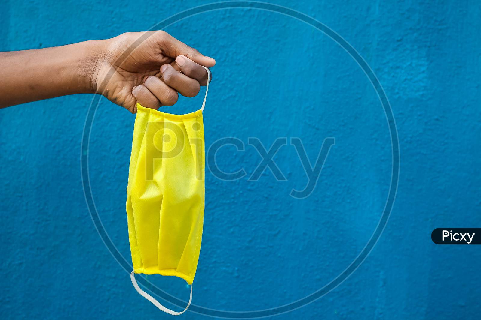 Man Holding Protective Yellow Face Mask Holding On His Hand Isolated On Blue Background