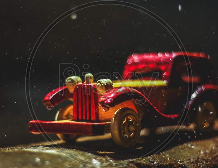 Vintage Toy Car Under The Rain On The Road. Miniature Car Toy In Rain. Red And Yellow Vintage Car On Rain. Rain Falling On Vintage Car Toy Close Up