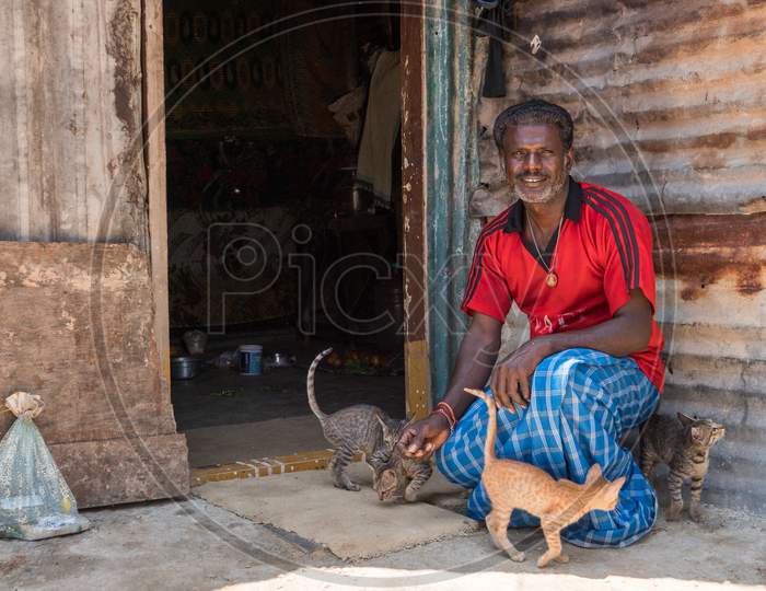 Bengaluru, Karnataka, India - November 08 2019: A poor Indian man with his cats and kittens in front of his makeshift shack in a slum