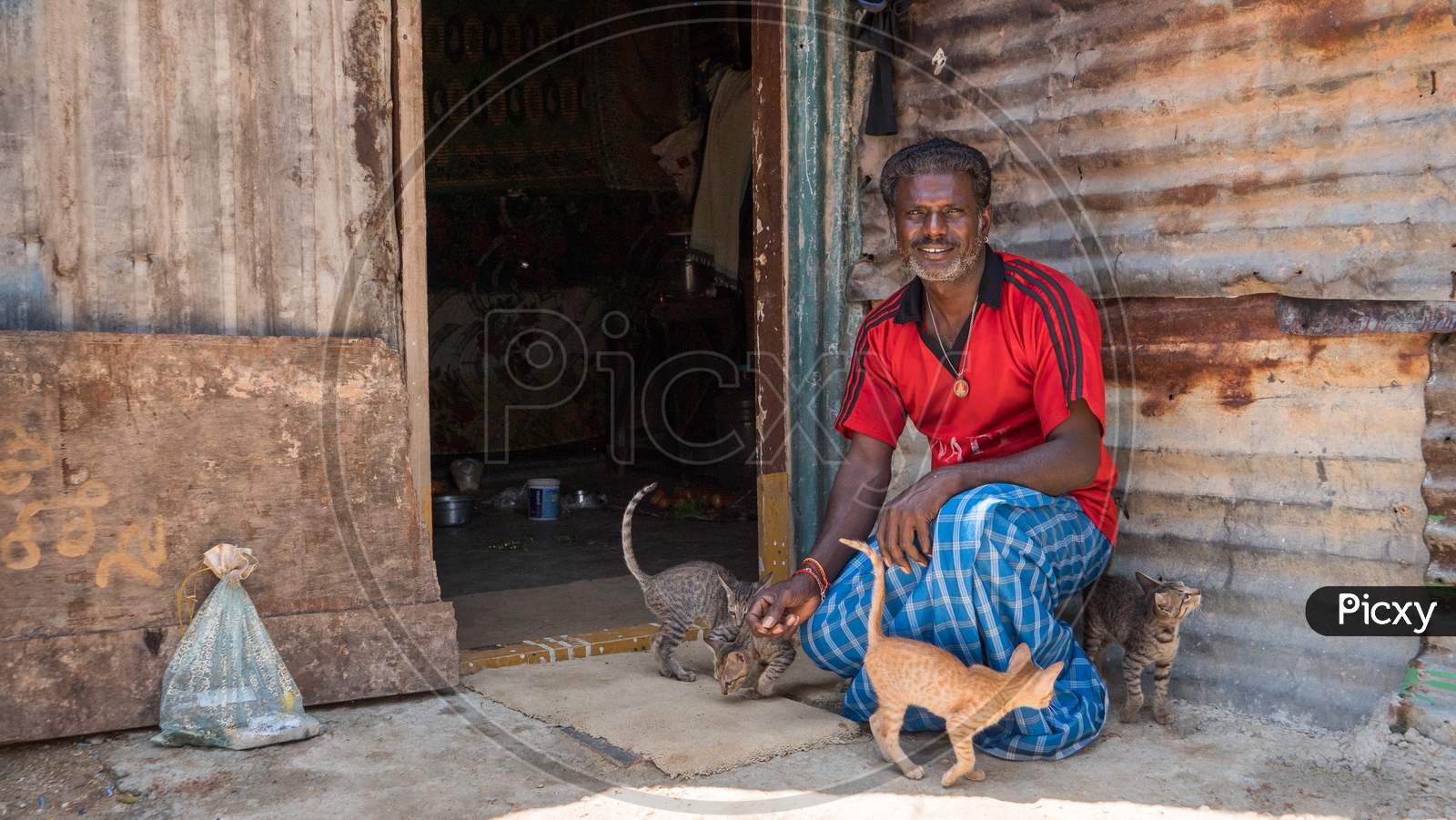 Bengaluru, Karnataka, India - November 08 2019: A poor Indian man with his cats and kittens in front of his makeshift shack in a slum