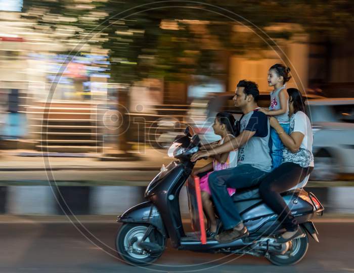 Bengaluru, Karnataka / India - August 02 2019: Grainy motion blur shot of a family of four riding on a scooter without wearing helmet dangerously