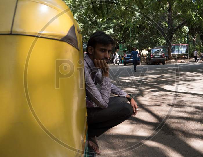 Bengaluru, Karnataka / India - March 01 2020: Medium wide angle shot of an autorickshaw from behind with the driver sitting sideways waiting for customer